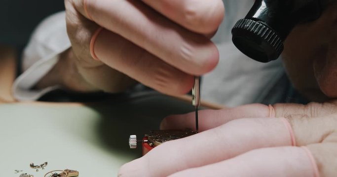 The Watchmaker Wearing An Eye Loupe Magnifier Unscrewing Carefully The Wristwatch Using A Small Screwdriver And Tweezer - Close Up Shot