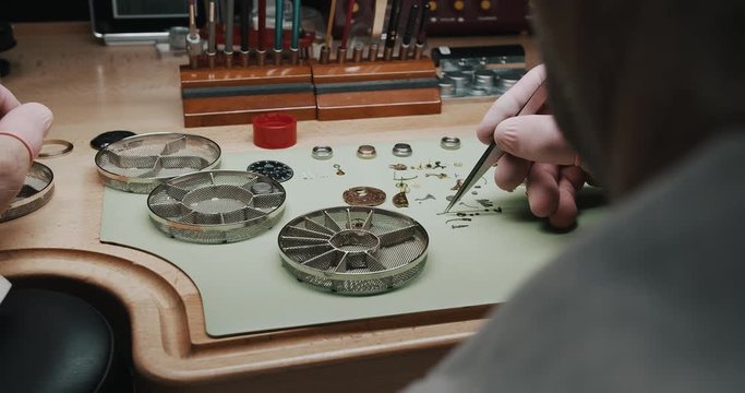 A watchmaker carefully putting tiny parts of a wristwatch into a metal screen container for cleaning - close up
