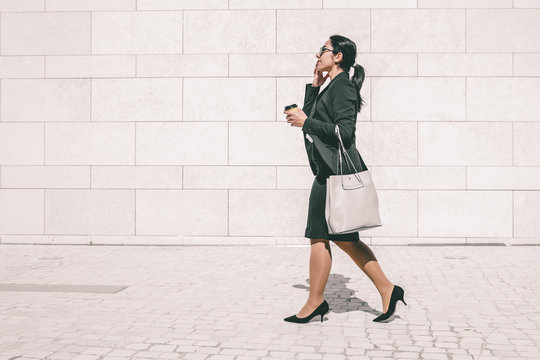 Serious Professional Late For Work An Drinking Takeaway Coffee On Run. Young Business Woman In Formal Suit Walking Outdoors, Carrying Handbag And Takeaway Coffee. Morning Way To Office Concept