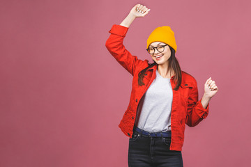 Having fun! Portrait of dancing happy young hipster woman in yellow hat and red shirt isolated over pink background.