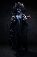 Portrait of woman witch in black clothes conjures on the dark background