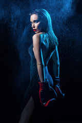 Back view of beautiful woman with bright makeup wearing dress and boxing gloves posing on dark background