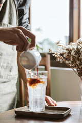 hand pouring espresso into an icy glass of tonic to make tonic coffee