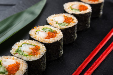 Sushi Rolls with shrimp on a dark background. Japanese traditional roll with prawn. Sushi set on a stone plate and dark concrete background. Sushi roll set and chopsticks. Fresh Japanese cuisine. asia