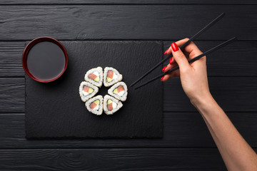 Woman holds sushi with chopsticks. Young woman holding sushi with a chopsticks, isolated on black. Sushi Roll with a woman hand holding chopsticks
