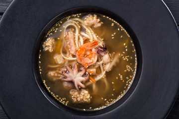 Seafood soup with squid, octopus, shrimp, eel, mussels, snails. Tom Yam soup with seafood. Spicy Asian Seafood Soup on black dish, thai cuisine.Bowl of fresh seafood soup.