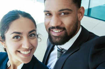 Happy business people taking selfie photo outdoors. Business man and woman looking at camera with building glass wall in background. Business people and selfie concept.