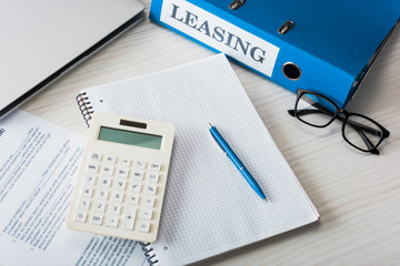 top view of folder with leasing lettering, pen, calculator and glasses near notebook on desk