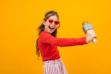 young singer with a microphone in her hands on a yellow studio background