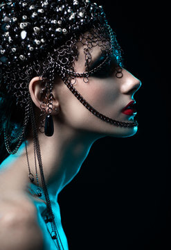 Portrait of attractive brunette woman in designer headdress with chains posing on dark studio background 