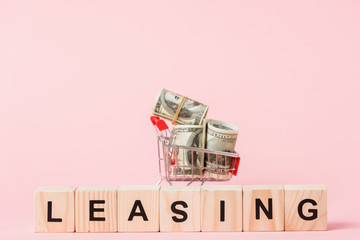 toy shopping cart with dollar banknotes near wooden cubes with leasing lettering on pink