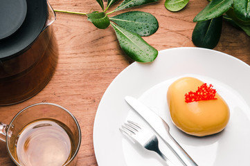 Closeup of gum paste mini cake with cup of tee on table. Delicious pastry on plate, teapot and green leaves on wooden table. Breakfast concept.