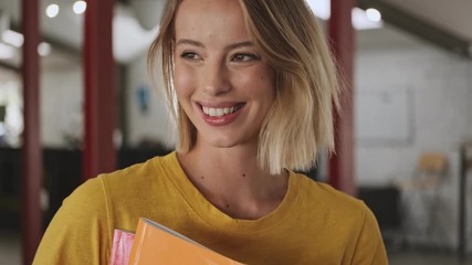 A close-up view of an attractive smiling young woman is holding a folders with files while standing in a conference hall
