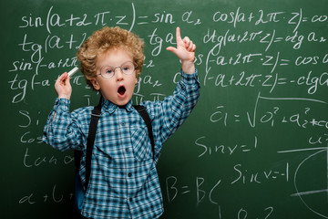 curly kid in glasses gesturing near chalkboard with mathematical formulas