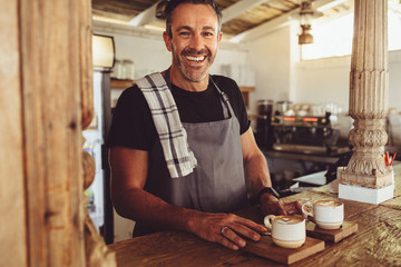 Male barista serving coffee to customers - obrazy, fototapety, plakaty