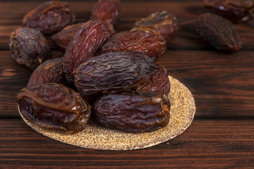 Tasty royal dates on a round substrate close-up on a wooden background