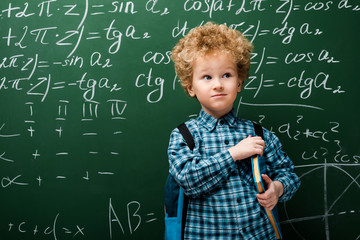 smart kid standing with book near chalkboard with mathematical formulas