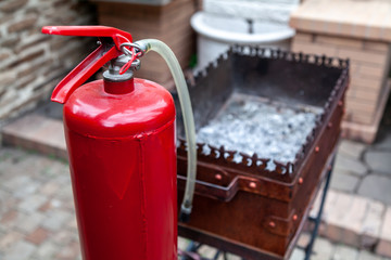 Red fire extinguisher stands on metal barbecue