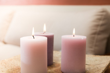 Fototapeta na wymiar Group of three burning candles in the home. Candles of pink tones in a warm house. Sofa in the background