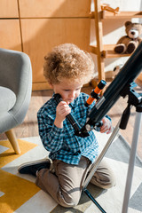 smart child touching telescope while sitting on carpet