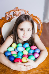 Fototapeta na wymiar A girl sits at a table and holds a plate of eggs for Easter, colored eggs, Easter and eggs, rabbits, a religious holiday