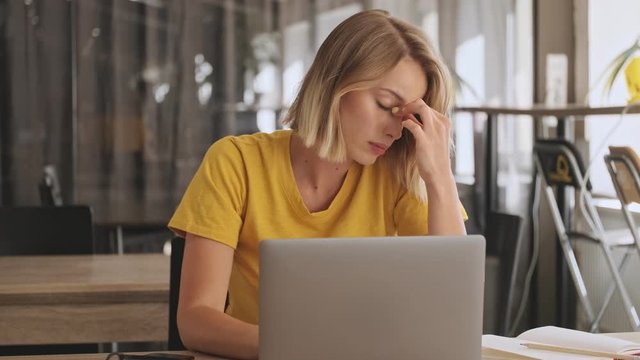A serious young woman is touching the bridge of her nose while working on her laptop in a conference hall