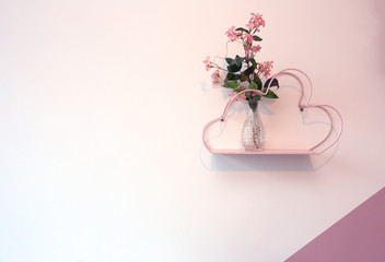 Decorative pink shelf on white wall with glass vase and pink bright flowers, modern romantic decoration interior