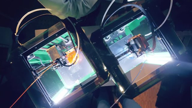 Top view of 3D-printers at work and a man with a computer. 3D printer printing an object from plastic