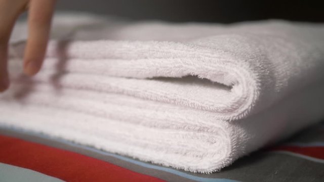 Close-up of hands putting stack of fresh white bath towels on the bed sheet. Room service maid cleaning hotel room macro closeup