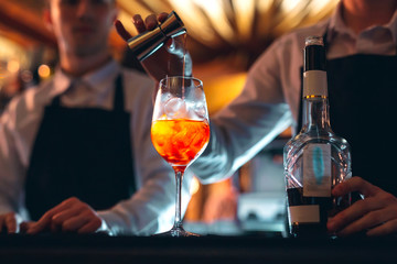 Barman hand stirring a fresh and sweet orange summer cocktail with a spoon on the bar counter. - obrazy, fototapety, plakaty