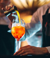 Barman hand stirring a fresh and sweet orange summer cocktail with a spoon on the bar counter.