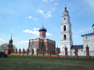 Church ensemble behind a mesh fence with a white stone bell tower and a red brick single-domed Church