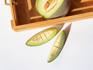 Pieces of green net melon fruit or honeydew and wooden crate top view on a white color table with sunlight.