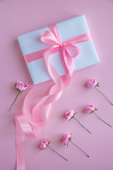 Gift or present box and flowers on pink table top view.