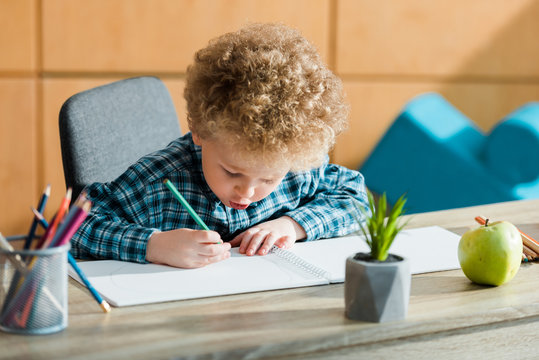 selective focus of smart and curly kid drawing near ripe apple on table