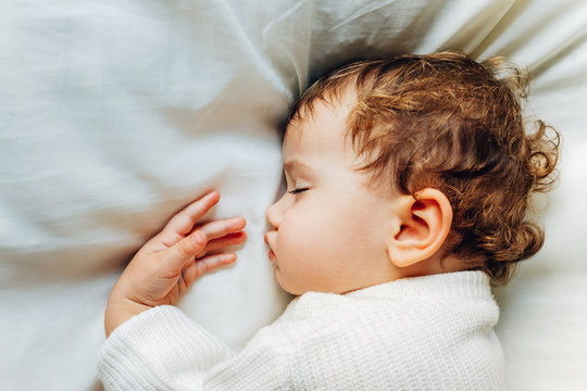 Baby Sleeps Peacefully During A Nap At Noon Lying On A Fluffy White Cushion.