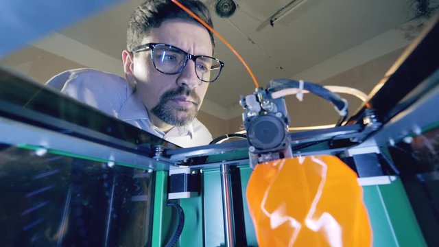 3D printer printing an object from plastic. Male engineer is looking inside of a 3D-printer making a vase