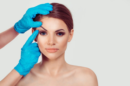 Upper eyelid blepharoplasty. Beautiful middle age woman getting ready for eyelid lift plastic surgery doctor hands in blue gloves point fingers to her eye on white. Beauty, people and health concept