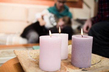 Three burning candles in the home. Candles of pink tones in a warm house. Young people on the sofa at the background