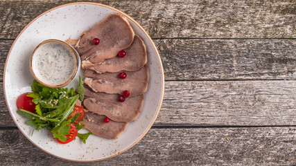 Copy space of sliced beef tongue with cranberry, horseradish sauce and green salad.  Rustic style. Top view