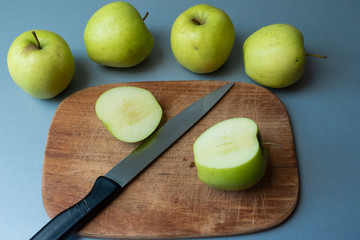 Green apples on rustic wooden cutting board with knife on kitchen countertop