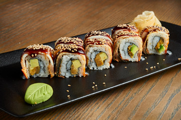 Appetizing sushi rolls - golden dragon. Rolls with eel, teriyaki sauce and avocado on a black plate on a wooden background. Film effect during post. Soft focus