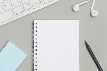Blank spiral notebook with keyboard, supplies and pencil on gray background. Top view office desk with notepad. Creative flat lay photo