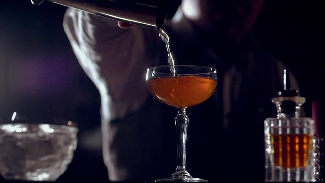 A prepared cocktail from a shaker is poured into a cocktail glass. It can be a Rob Roy cocktail, Old Pal cocktail or another. Dark scene, slow motion