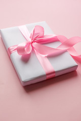 A white gift box with a long pink ribbon is lying on a pink table