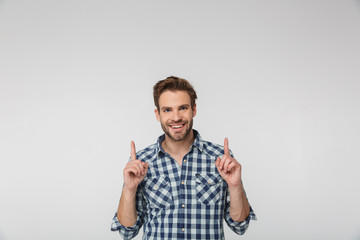 Portrait of joyful young man smiling and pointing fingers upward