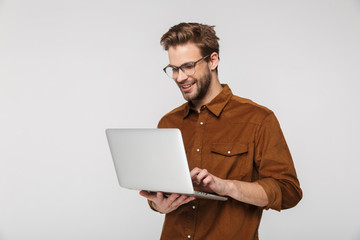 Portrait of cheerful young man using laptop and smiling - obrazy, fototapety, plakaty