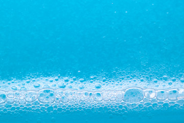 Transparent foaming blue liquid with oxygen bubbles texture close up. Abstract surfactant cosmetic background. SLS free concept