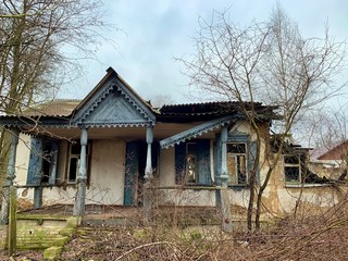 Abandoned house on an empty plot. Ruined building among trees and shrubs. Old, abandoned house in the park against the sky.
