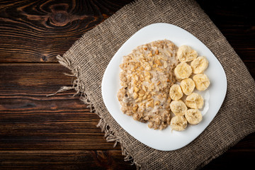 Oatmeal with banana and peanut on dark wooden background.
